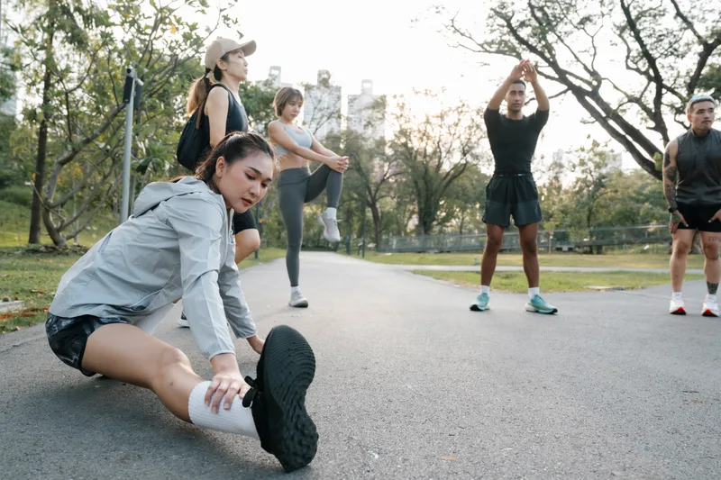 Group of runners stretching and warming up on a tree-lined park path in early morning light