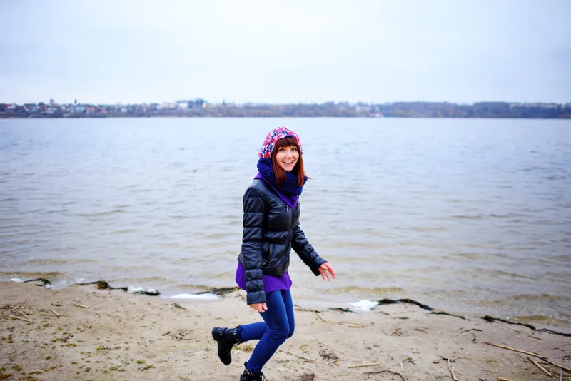 Person in a knitted toque and warm jacket walking along a lakeshore beach on an overcast winter day