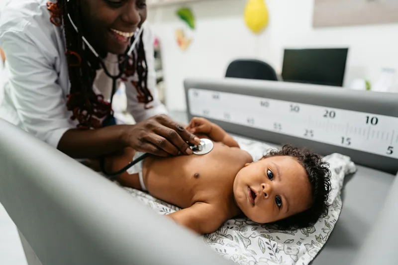A smiling clinician listening to a calm baby's chest with a stethoscope in an Orléans exam room