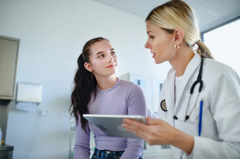 A clinician with a tablet talking through results with a teenage patient in a bright exam room