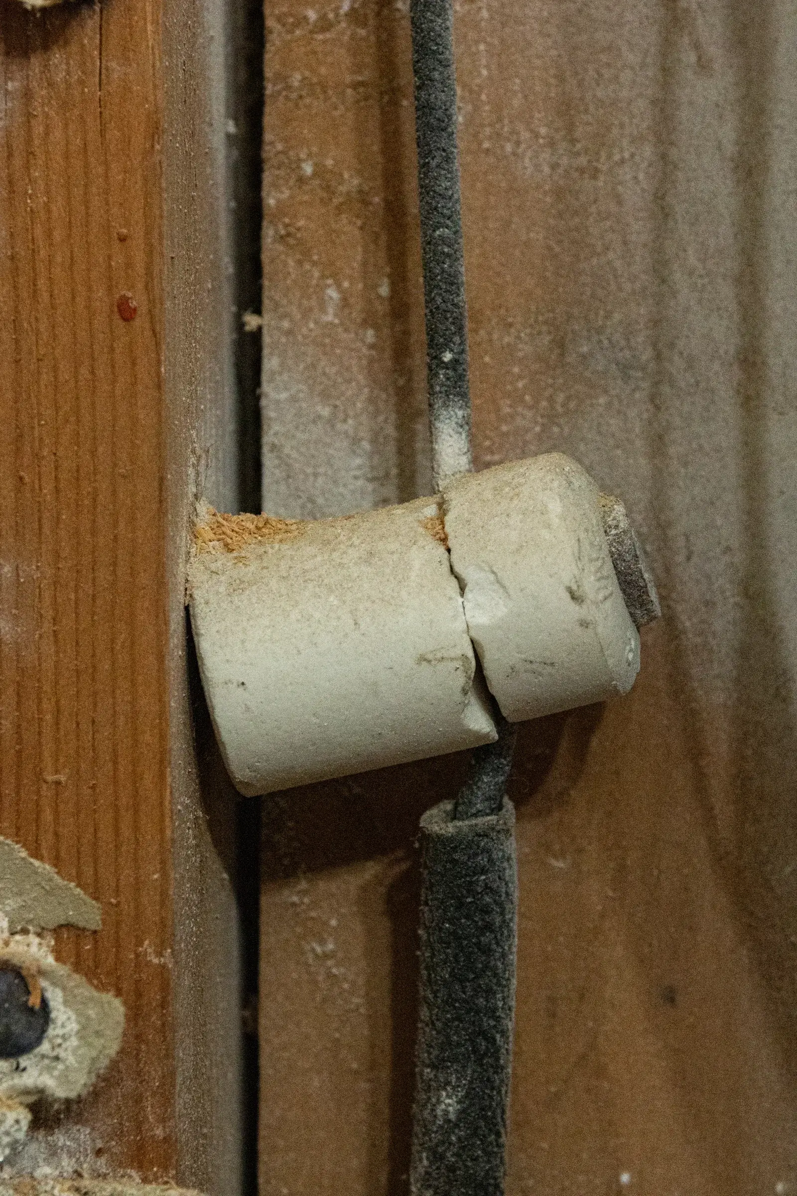 Close-up of a ceramic knob supporting original cloth-insulated knob-and-tube wiring against old house framing