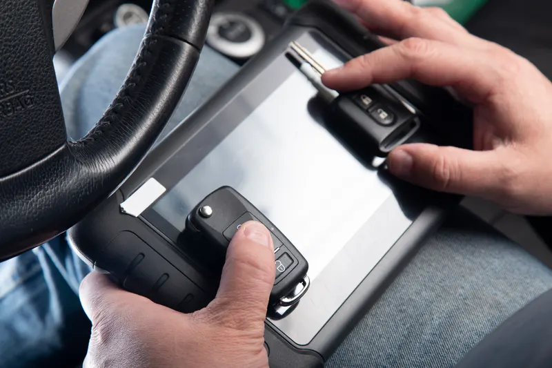 Automotive locksmith programming two replacement key fobs with a diagnostic tablet in the driver's seat