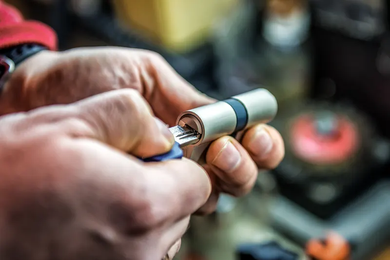 Locksmith's hands repinning a lock cylinder at a workbench — the same hardware, a brand-new key