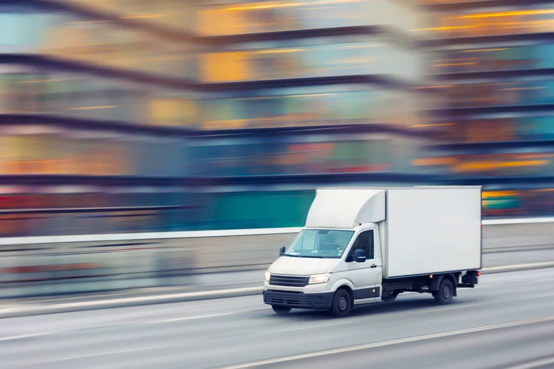 Service box truck moving fast through city streets, background blurred with speed