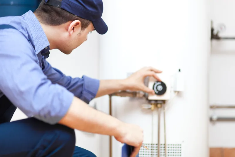Technician in a blue uniform adjusting the gas control valve on a tank water heater