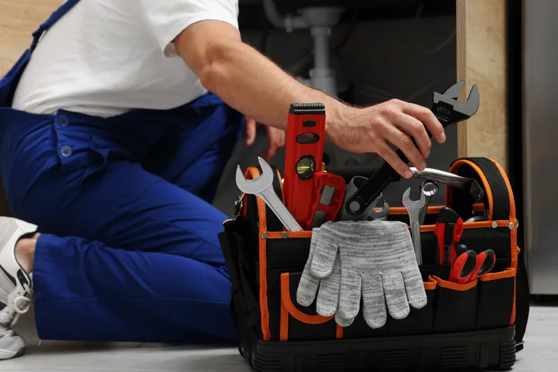 Technician kneeling beside a fully stocked open tool bag with wrenches, level, and work gloves