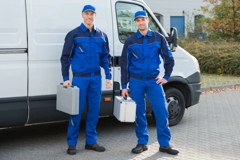Two Cascade technicians in blue uniforms standing with tool cases beside a white service van