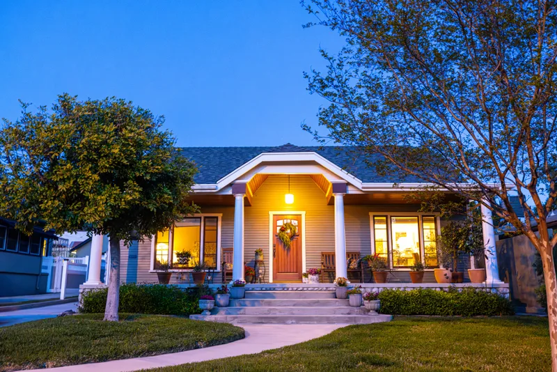 Freshly painted single-storey craftsman bungalow at dusk with grey siding, white trim and a red front door