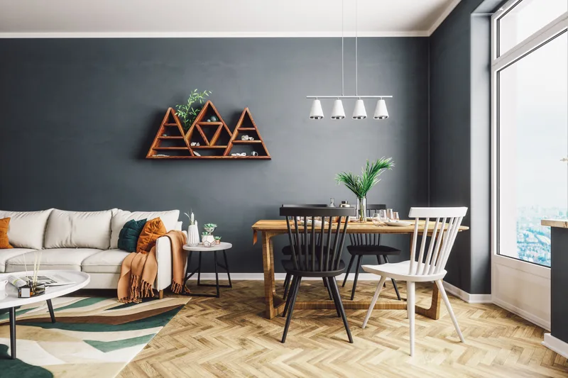 Open dining and living room with one deep charcoal painted wall, white trim, a wood table and herringbone floor