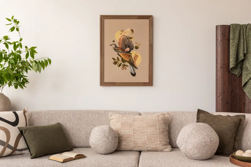Calm living room with warm white walls, a framed bird print and a soft beige sofa with patterned pillows