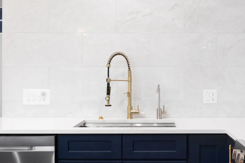 Kitchen with lower cabinets painted deep navy, white quartz counter and a brushed gold faucet