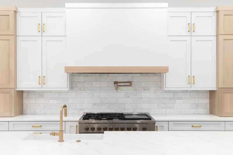 White painted kitchen cabinets and walls with a white oak range hood and brass hardware