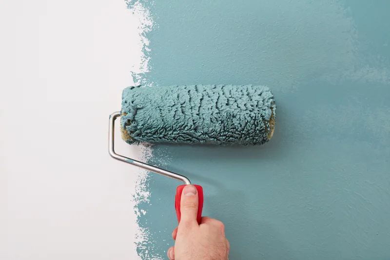 Close up of a paint roller laying a fresh coat of teal over a white wall