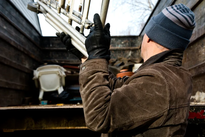 Gloved crew member lifting a bundle of scrap metal tubing into the open box of a junk removal truck
