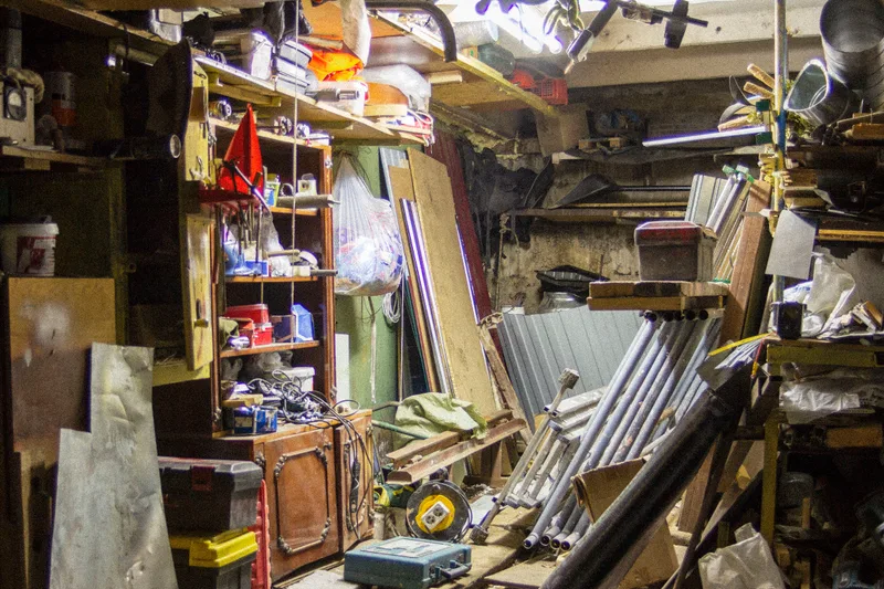 Overstuffed suburban garage packed floor to ceiling with shelving, lumber, bins, tools, and years of accumulated clutter