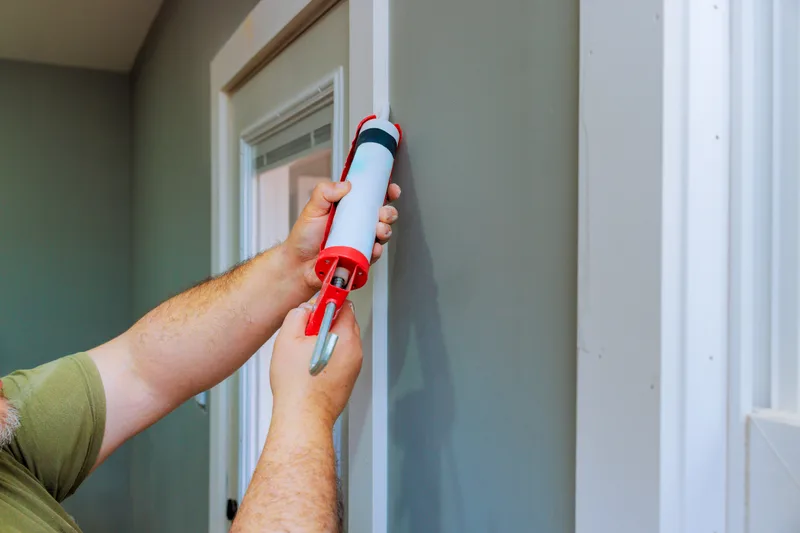Hands sealing the gap along a door frame with a caulking gun — exclusion work that keeps pests out without any product