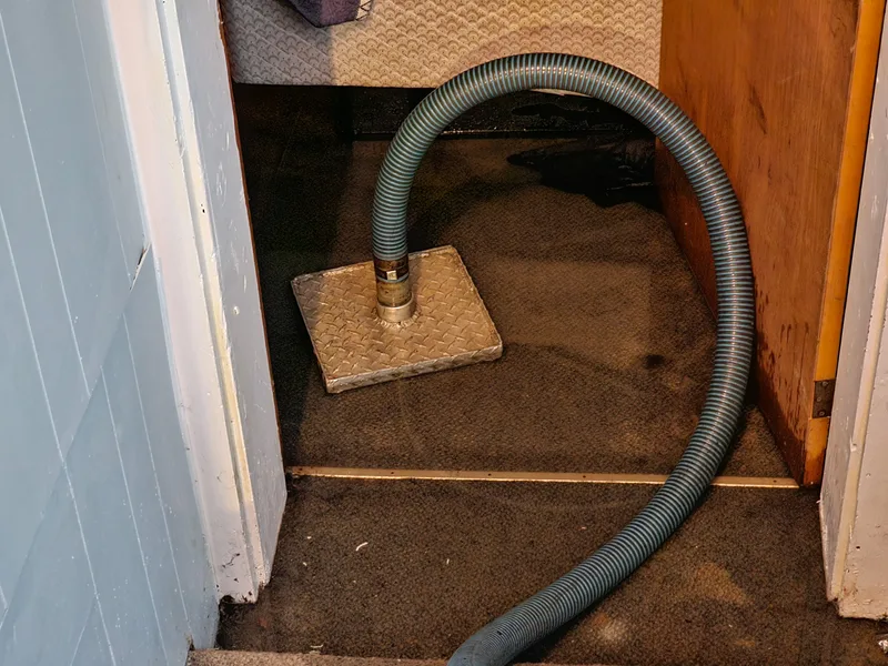Extraction hose running through a basement doorway to pump out water from a flooded floor