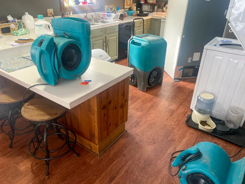 Teal air movers and a dehumidifier drying a kitchen after a water leak