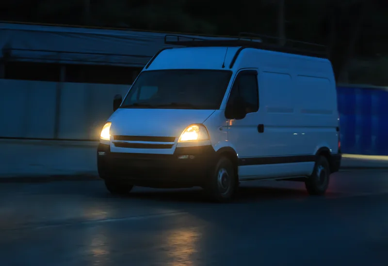 White service van with its headlights on, parked on a street at night