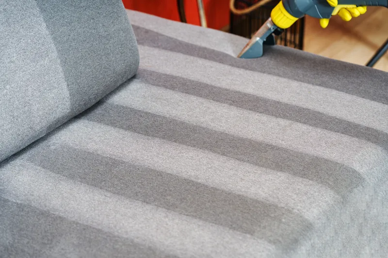 Upholstery cleaning wand lifting a clean stripe across a grey sofa cushion