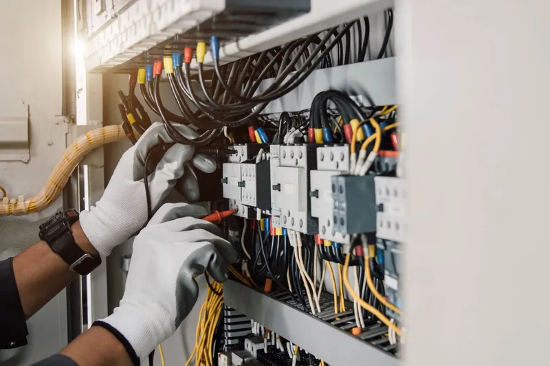 Gloved hands working on labelled wiring and contactors inside an electrical control panel