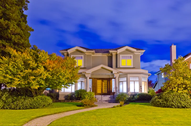 A two-storey house at dusk with warm light in the windows and a curved front path