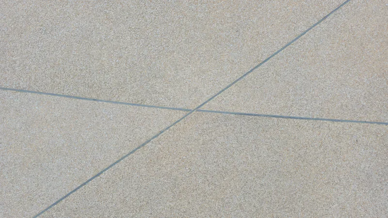 Close view of exposed aggregate concrete with thin saw-cut control joints crossing it