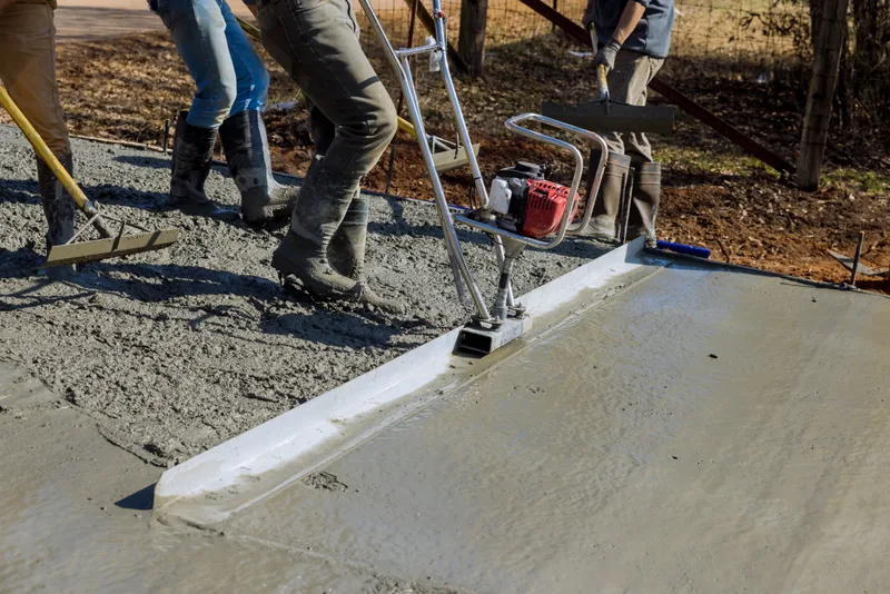 Crew placing fresh concrete for a driveway while a finisher runs a power screed along the form