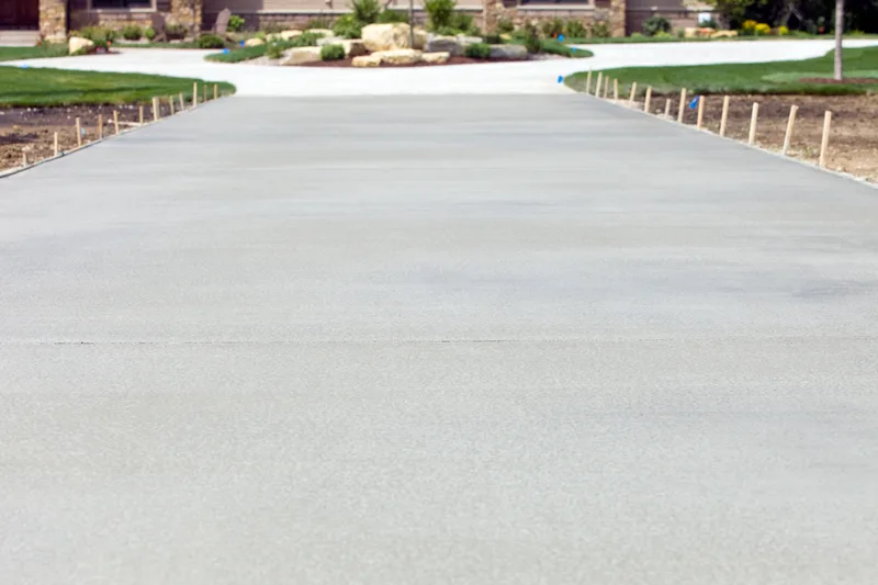 Long, new light-gray concrete driveway curving up to a house, with landscaping on both sides