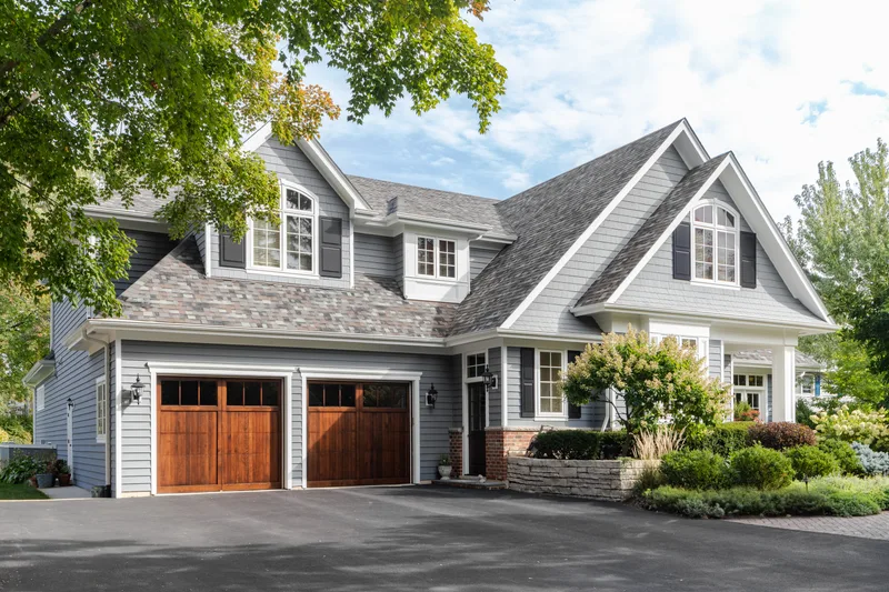 Gray and white two-story house with white windows, dormers and two wood garage doors