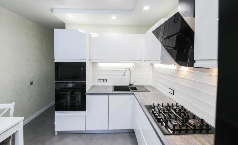 Modern white kitchen with a built-in wall oven, gas cooktop and range hood