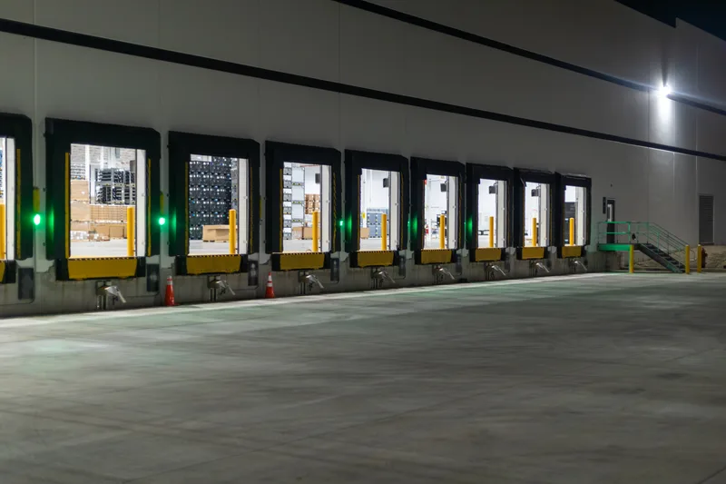 Row of warehouse loading dock doors lit at night beside an empty concrete apron