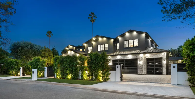 Modern dark home at dusk with lit dark glass garage doors