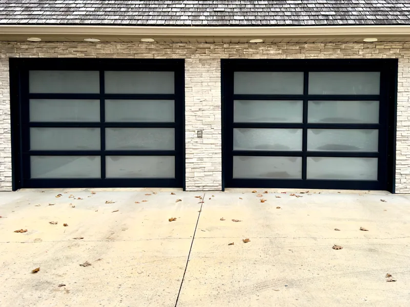 Two black-framed full-view garage doors with frosted glass in a stone wall