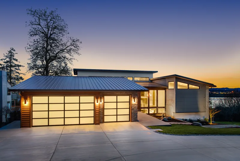 Modern home at dusk with a three-car full-view glass garage door glowing warm from inside
