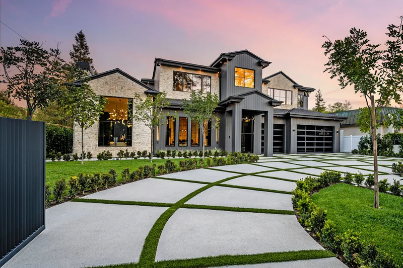Modern two-story home at sunset with dark flush garage doors and a geometric driveway