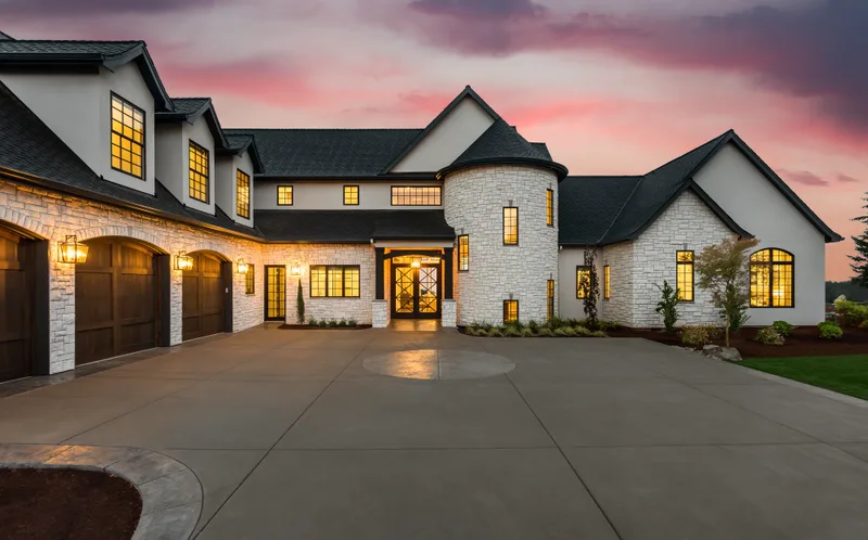 Stone house at dusk with three dark carriage garage doors and lit windows
