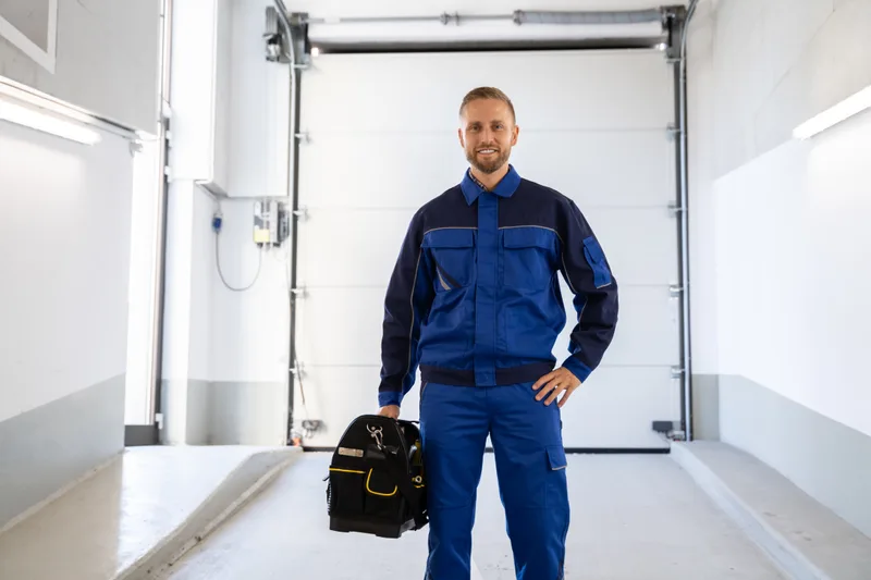 Smiling Liftline technician in a navy uniform holding a tool bag inside a garage