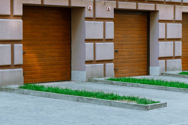 Two warm wood-look steel garage doors in a light stone building