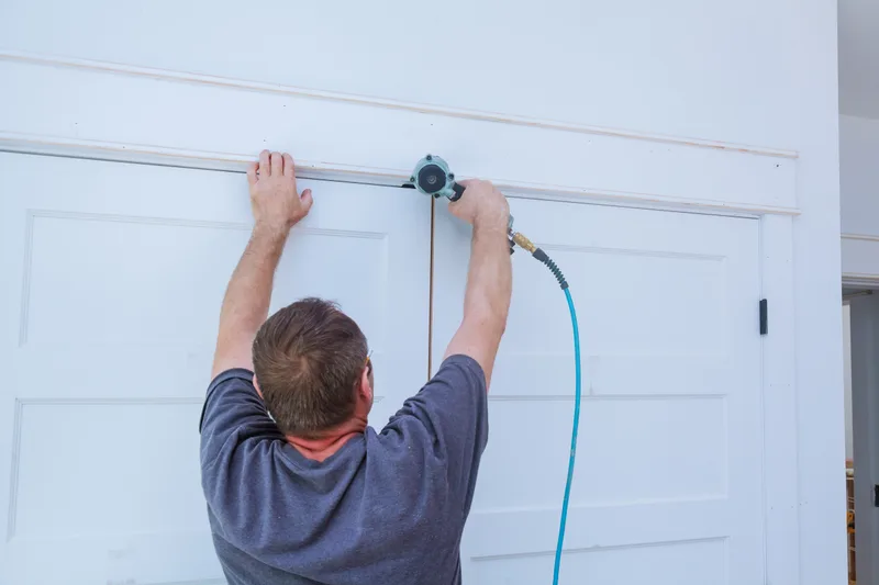 Carpenter fastening trim above a white door with a brad nailer
