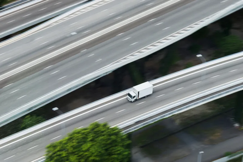Aerial view of a single white moving truck traveling an open interstate between overlapping highway ramps