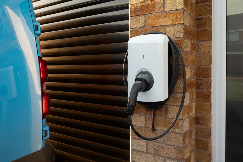 Wall-mounted Level 2 EV charger with a coiled cable on a brick wall beside a garage door