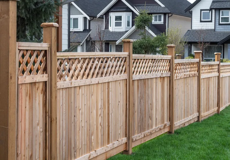 New cedar privacy fence with a lattice top and capped posts along a row of suburban homes