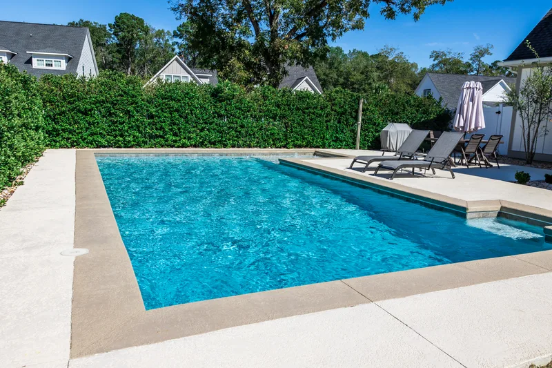 Newly finished rectangular pool with tan concrete coping and a broom-finish deck in a hedged backyard