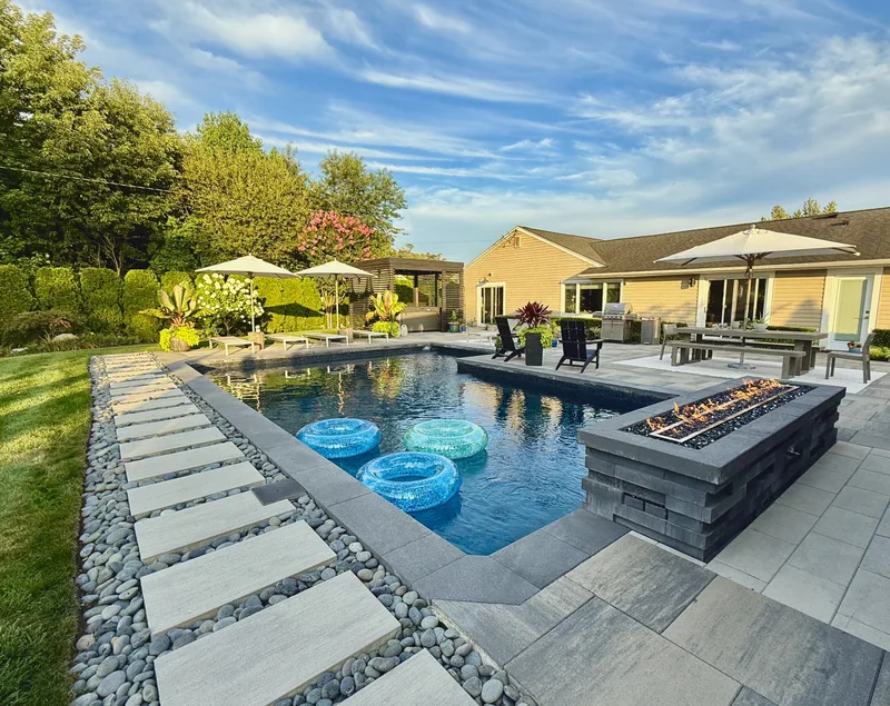 Geometric pool with a raised fire feature, large stepping pads set in river rock and a stone patio