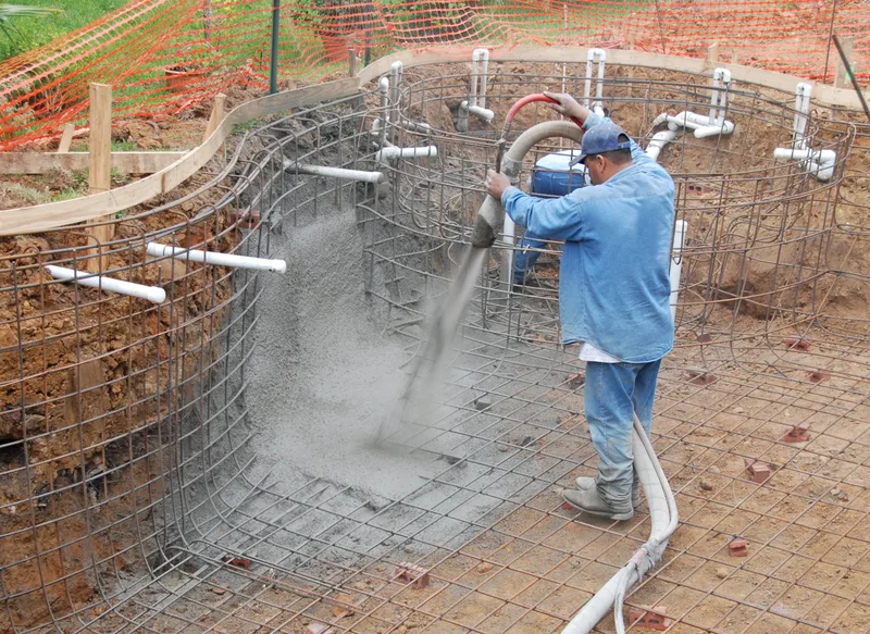 A crew member sprays gunite over the steel rebar cage of a curved pool