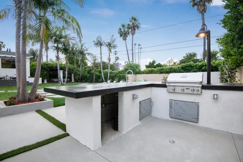 Outdoor kitchen island with a built-in grill and concrete counter, palm trees behind