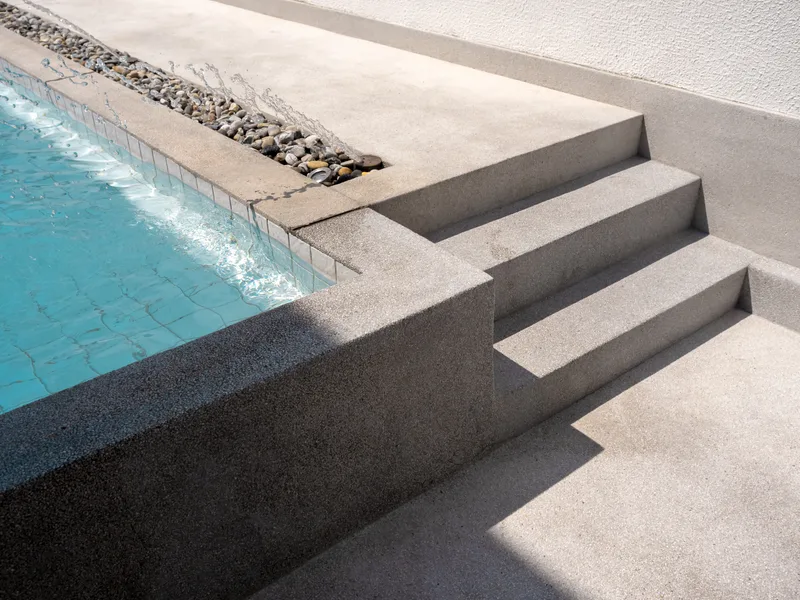 Close view of new pool steps and an exposed aggregate deck beside a sheer water feature