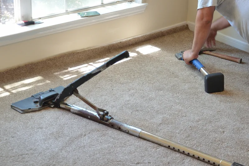 Carpet installer using a power stretcher on new beige carpet in a sunlit room