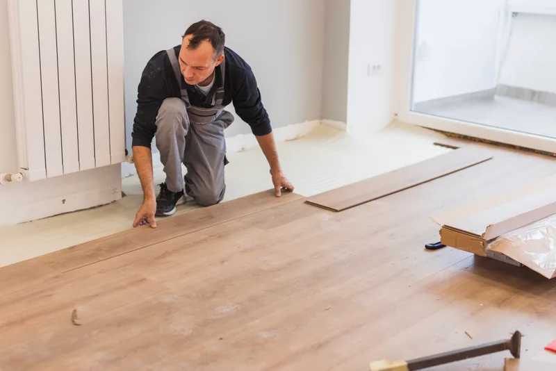 Installer kneeling to click light wood-look floating planks into place over foam underlay